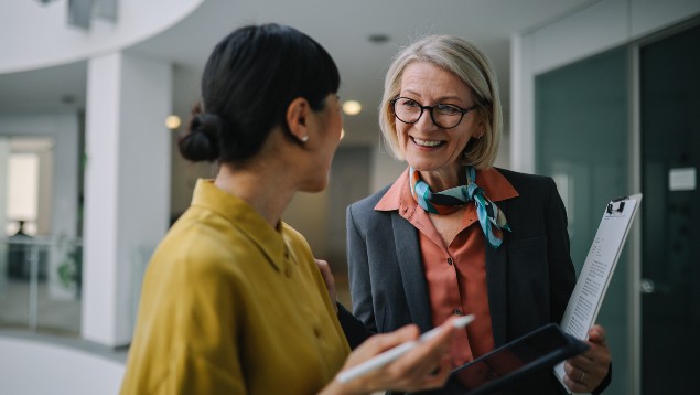 Two professional women talking in the hallway holding tablets
